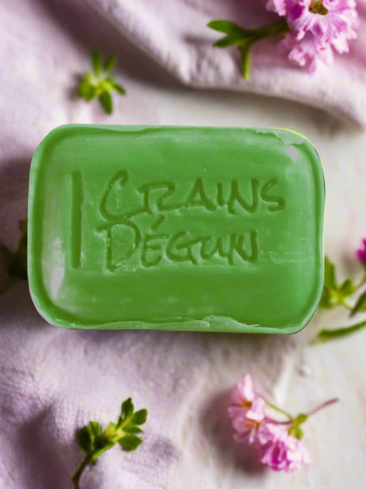 Green bar soap with crains degun engraved in the middle of the soap surrounded by verbana flowers on a light purple cloth