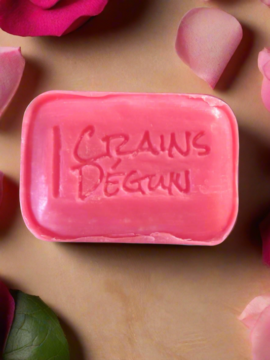 pink bar soap with crains degun engraved in the middle of the soap bar on a beige background with rose petals around the soap